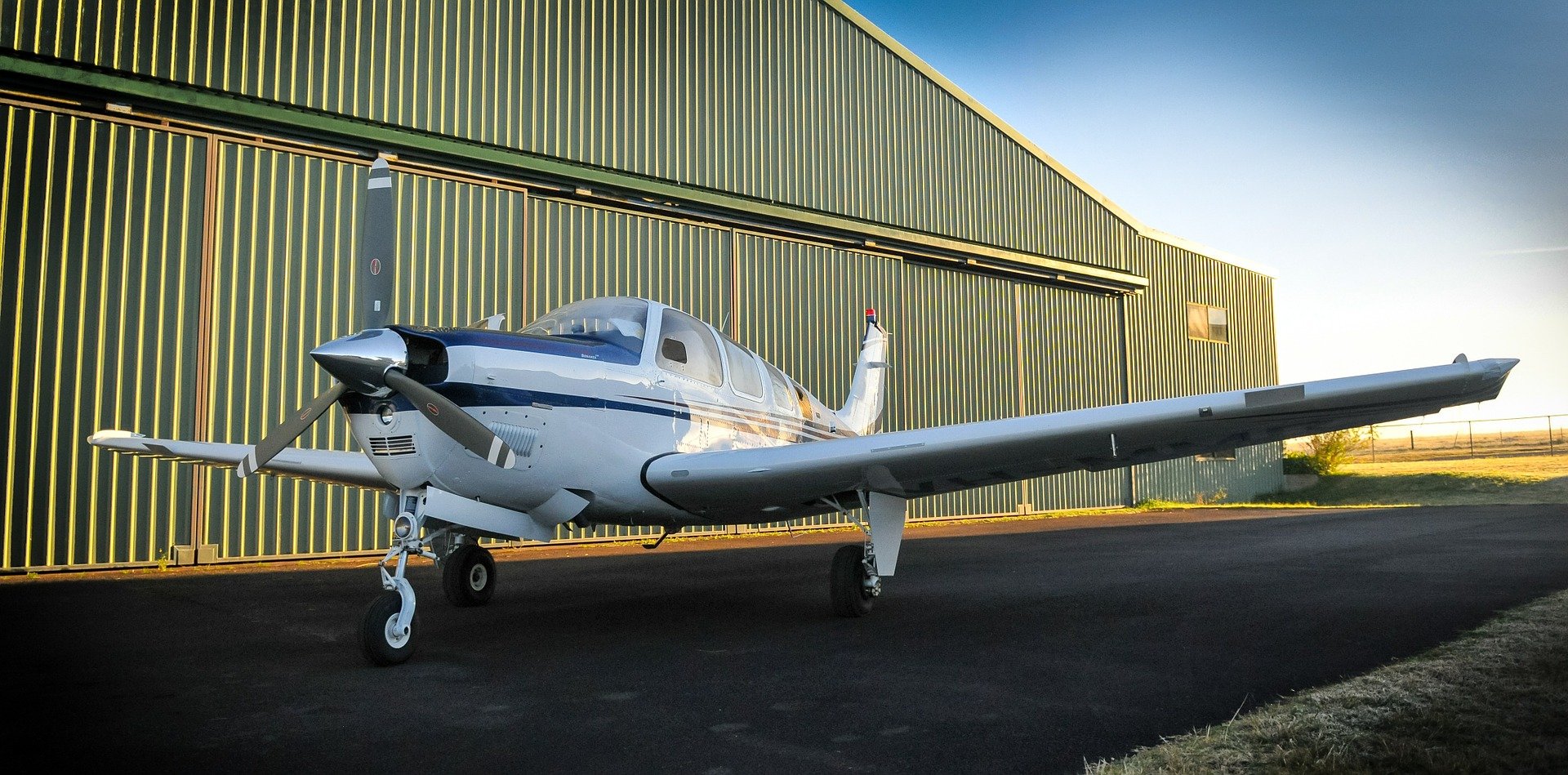 Propeller aircraft parked alongside a sunlit hangar